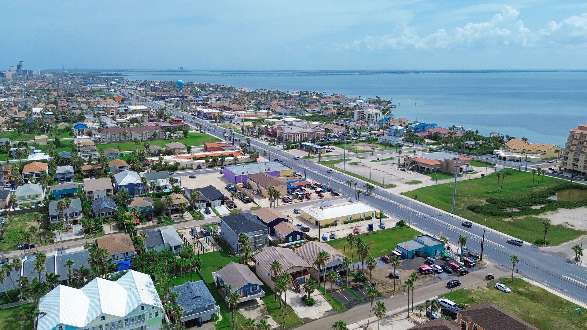 Downtown South Padre Island boulevard with palm trees, row of colorful painted beach houses, waterfront condos, resort, hotels, vacation rentals along Laguna Bay, travel destinations, aerial
